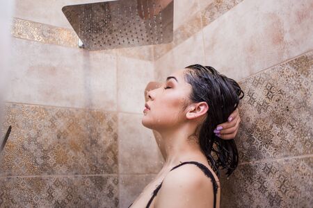 Woman taking a shower enjoying water splashing on her in the bathroomの写真素材