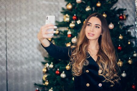 Cheerful young woman taking a Christmas selfie with smartphone. Holiday, New year, happiness conceptの写真素材