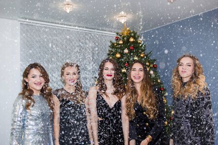 New year, holiday, celebration, party concept. A group of beautiful glamorous women with bright makeup and dresses on the background of Christmas trees and confettiの写真素材