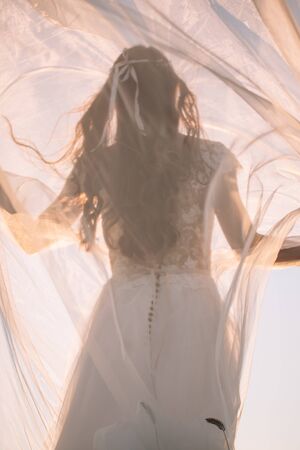 Beautiful silhouette of a woman bride in a long white dress and veil in the afternoon at sunset against the blue skyの写真素材