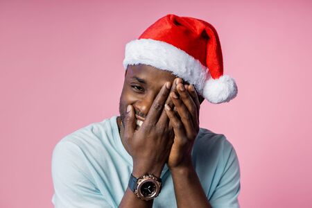 Cheerful curious african american man with bristle, hiding face with hands, peeking through fingers, feeling shy, waiting surprise, isolated over pink background. Emotions concept.の写真素材