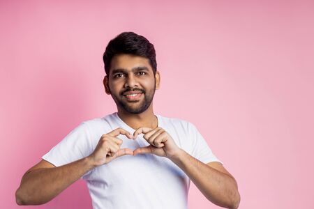 I love you. Happy cheerful unshaven man showing heart gesture over chest, cute smiling, expressing his love and affection to girlfriend, isolated over pink background. Body language, feelings.の写真素材