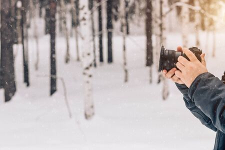 Close-up of the photographer's hand on the background of a winter forest with snowfall. Copy space. Professional equipment, camera, stabilizer for video shootingの写真素材