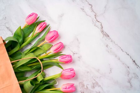Closeup of beautiful pink tulips in a craft paper bag on a marble white background with copy space, top view. Spring, summer, flowers, color conceptの写真素材
