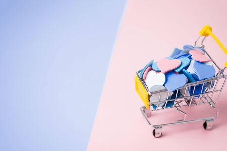 Closeup of a miniature shopping cart full of colorful hearts on a two tone ink and blue background....