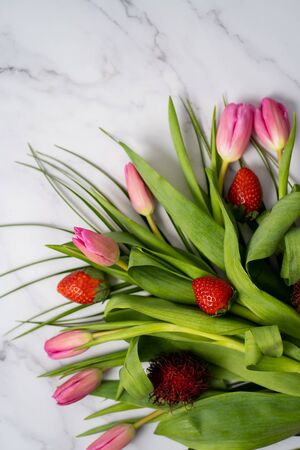 Closeup of a beautiful bouquet of flowers with red strawberries on a marble table with copy space for text. Spring, summer, tulipsの写真素材