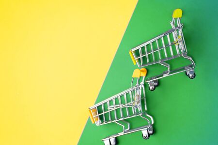 Supermarket, mall, market, shopping, sale concept. Two empty miniature toy trolley on yellow and green background, copy space for text or design. Flat lay, top view.の写真素材