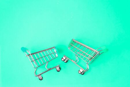 Two small miniature metal supermarket trolleys for shopping isolated on bright mint colour trendy background. Top view. Copy space for text. Shopping, purchases, sale concept.の写真素材