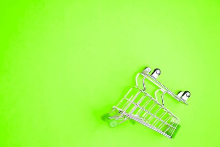 Top view, flat lay shot of shopping cart on bright green background. Copy space for text or design. Stainless steel shopping trolley upside down. Minimalist shopping concept.の写真素材