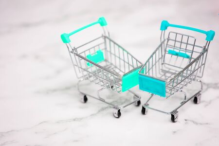 Two empty metal small miniature toy shopping trolley on white marble background. Shopping, supermarket, sale concept. Collection of shopping carts.の写真素材