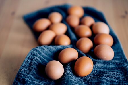 Brown fresh chicken eggs on blue kitchen towel. Pile of eggs on wooden table. Concept of farm...