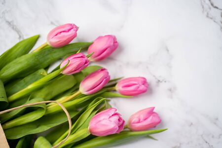 Closeup of beautiful pink tulips in a craft paper bag on a marble white background with copy space, top view. Spring, summer, flowers, colorの写真素材