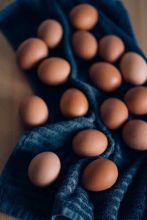 Brown fresh chicken eggs on blue kitchen towel on wooden table. Concept of farm products, natural food, healthy eating, easter. Vertical shot.の写真素材