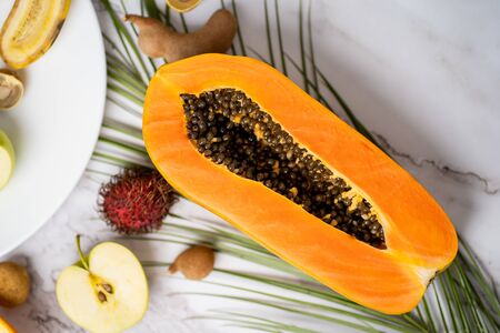 Closeup of half of ripe fresh papaya with seeds, longan, tamarind, rambutan on marble table. White background with copy space for text. Food, summer and healthy eating concept . Top view.の写真素材