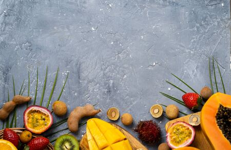 Top view of tropical fruits on grey blue background with free space for your text. Set of dragon fruit, rambutan, tamarind, mango, passion fruit, kiwi, orange, strawberry, leaves. Flat lay.の写真素材