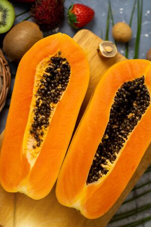 Papaya. Tropical Fruits. Close up shot of two halves of ripe papaya with seeds on wooden cutting board. Sliced papaya and other exotic fruits on table. Top view.の写真素材