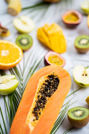 Assorted ripe juicy fresh tropical summer seasonal fruits and tropical leaves on white background. Exotic asian fruits. Sliced fruits on table. Selective focus. Vertical shot.の写真素材