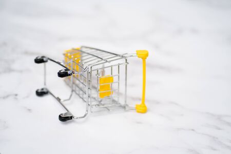 Empty inverted shopping cart on white marble background. Stainless steel small miniature toy shopping trolley on table. Business, mall, market, shopping concept.の写真素材