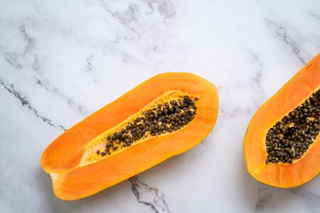 Closeup of halves of ripe papaya fruit with seeds. Ripe fresh papaya fruit on white marble table. Top view. Horizontal shot. Vegan diet, exotic fruits, food concept.の写真素材