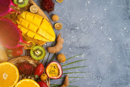 A set of papaya, dragon fruit, rambutan, tamarind, mango, passion fruit, kiwi, orange, strawberry, green leaves on gray stone background with copy space. Flat lay, top view summer composition.の写真素材