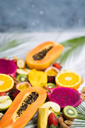 Summer composition from different sliced exotic fruits and tropical leaves. Fresh sliced apple, mango, orange, kiwi, papaya, maracuja, dragon fruit, rambutan, longan on table. Healthy food.の写真素材