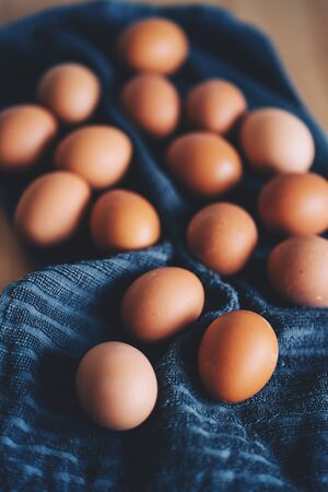 Brown fresh chicken eggs on blue kitchen towel. Pile of eggs on wooden table. Concept of farm products, natural food, easter. Protein food. Selective focus.の写真素材