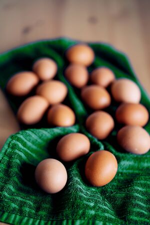 Brown fresh chicken eggs on green kitchen towel. Pile of eggs on wooden table. Concept of farm products, natural food, easter. Protein food. Selective focus.の写真素材