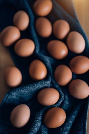 Flat lay image of eggs on blue kitchen towel. Raw chicken brown eggs on wooden background with copy space for text. Minimalist style. Farm products, protein food, easter concept.の写真素材