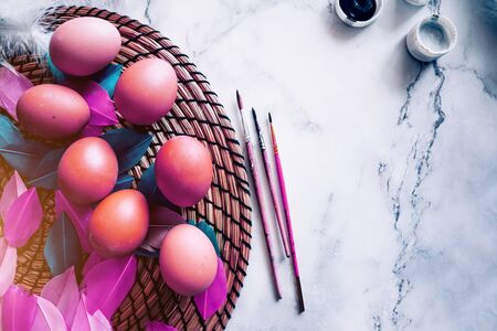Colorful spring easter background with colored purple eggs, white feathers, dyes, brushes on light marble table. Copy space, top view. Happy Easter concept.の写真素材