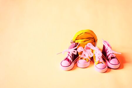 Two pair of small sneakers and yellow backpack isolated on light peach background with empty space for text or design. Miniature baby shoes and bag. Sport style, children, shoes store concept.の写真素材