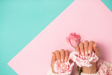 Closeup beautiful pink flowers on women's hands with manicure on nails on colored background with copy space. Care, beauty, Spa, salon conceptの写真素材