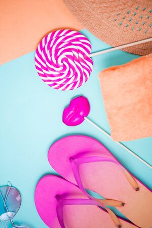 Flat lay of pink flip flops, Lollipop in the shape of lips and circle sunglasses, towel and hat on a bright blue background with copy spaceの写真素材