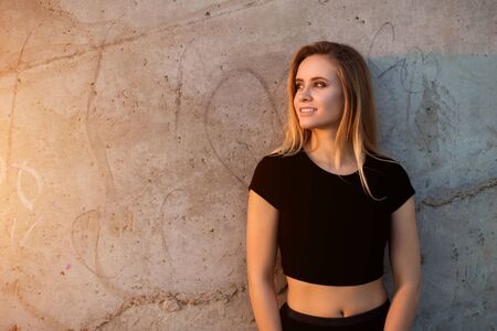 Horizontal portrait of beautiful smiling blonde woman on outdoor wall background with copyspace. The girl looks to the sideの写真素材