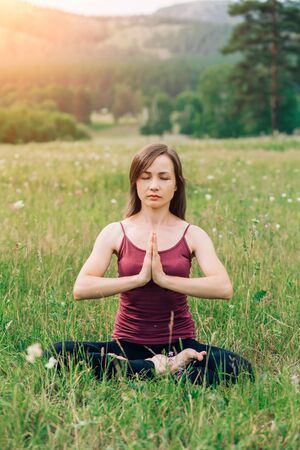 Lifestyle portrait of a beautiful young woman in a yoga position on the background of natureの写真素材