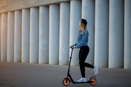Beautiful young woman riding a scooter on the asphalt. Sports, walking, leisure, entertainment, Hobbies, summer conceptの写真素材