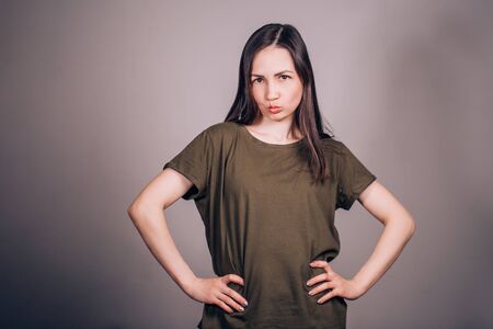 Beautiful young girl making a face, makes a grimace to the lips and charismatically looking into the camera on gray background. Positive human emotions.の写真素材