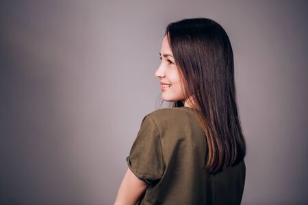 Beautiful young woman standing sideways on grey background, and laughs, smiles. The profile of the...