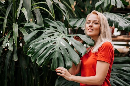 Profile portrait. Closeup of blonde haired beautiful caucasian girl posing before leaves of monstera in tropical forest. Attractive model with healthy skin. Purity, wellness and skincare.の写真素材