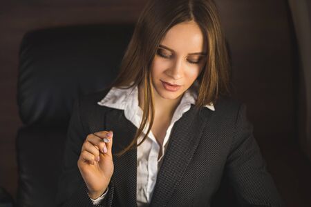 Beautiful successful brown-haired young businesswoman wearing black suit, using tablet, smiling while sitting in the chair of her private business plane. Flying first class.の写真素材