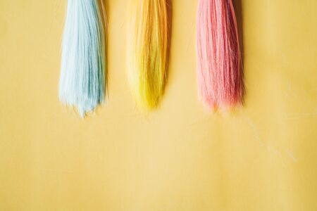 Multicolored straight long hair, wigs for handmade dolls on yellow background. Handwork, hobby, leisure concept. Top view. Colored strands of hair.の写真素材