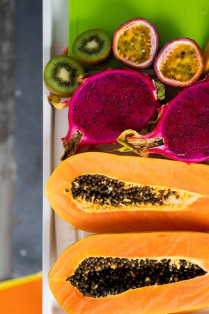 Assortment of sliced tropical exotic fruits on white tray. Top view. Close up. Healthy vegan breakfast of raw papaya, orange, mango, dragon fruit, kiwi, maracuja. Summer, food concept.の写真素材