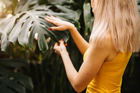 Closeup side portrait of a blonde woman in a yellow bathing suit on a background of exotic woods and the leaves of the monstera. Cropped photoの写真素材