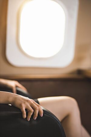 Cropped vertical shot of businesswoman with flight fear in private jet. Selective focus of terrified woman sitting clutching the arms of the chair in private plane. Aerophobia concept.の写真素材