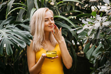 Beautiful caucasian blonde woman with healthy smooth clean skin holding jar of body creamの写真素材
