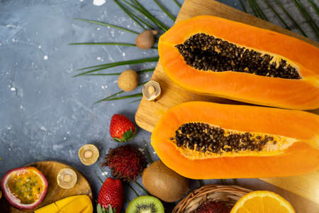 Papaya. Tropical Fruits. Close up shot of two halves of ripe papaya with seeds on wooden cutting board. Sliced papaya and other exotic fruits on table. Top view.の写真素材