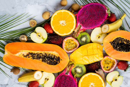 Assortment of different sliced exotic fruits with tropical leaves on table. Top view. Vertical shot. Healthy lifestyle, food, dieting, vacation, summer seasonal fruits concept.の写真素材