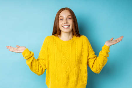 uncertain ginger woman with perplexed expression, frowning face, spreading hands with confused look isolated over blue background. Expressive face expression and emotions.の写真素材