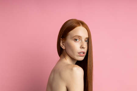 Headshot closeup portrait of serious caucasian female model with freckles, red hair, clean skin, bare shoulders, without makeup looking at camera with calm expression. Natural beauty concept.の写真素材