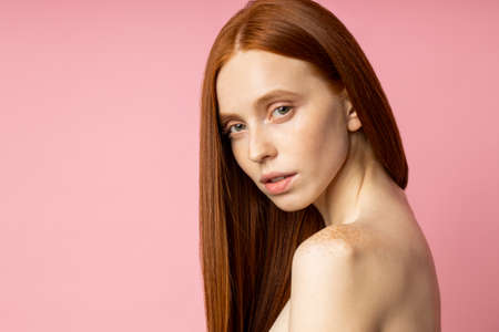 Studio portrait of sensual young woman with red long hair over pink background. Pretty naked caucasian female model with freckled fresh clean skin. Beauty and skin care concept. copy space for text.の写真素材