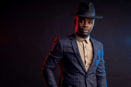 serious unshaven african businessman, wearing shirt, checkered suit standing against dark backgroundの写真素材
